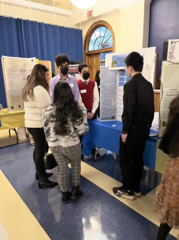 Senior Massimo Bragna presents his research poster to a judge alongside his group members. 