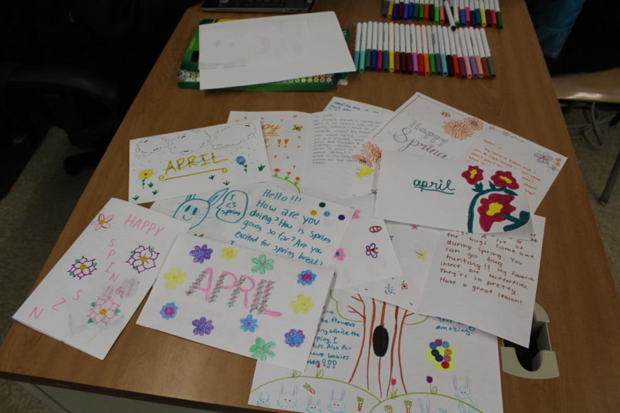Club members final cards cover the table, full of vibrant colors, ready to be sent out to orphans digitally. 

