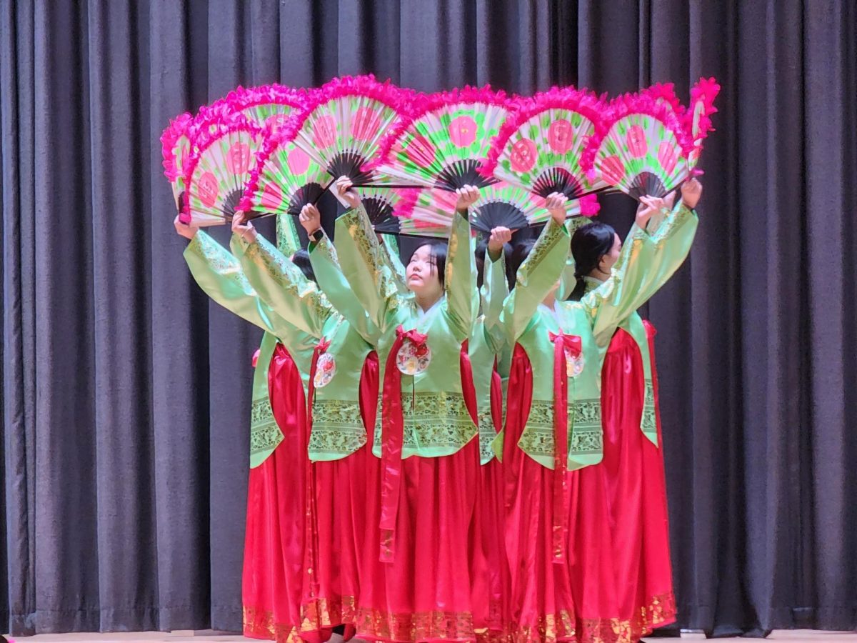 Korean language students Genesis Kim (front left), Sarah Kim (front center), and Da-eun Kim (front right) and other students performing neoclassical Korean fan dance “Buchaechum”. Which is a dance usually performed by a group of female dancers wearing colorful and flowing Hanbok dance to Minyo (Korean folk music).
