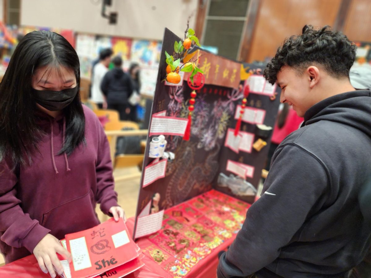 A FLHS student interacting with a presenter at a “fortune telling” station that tells them their Chinese Zodiac according to their age. 